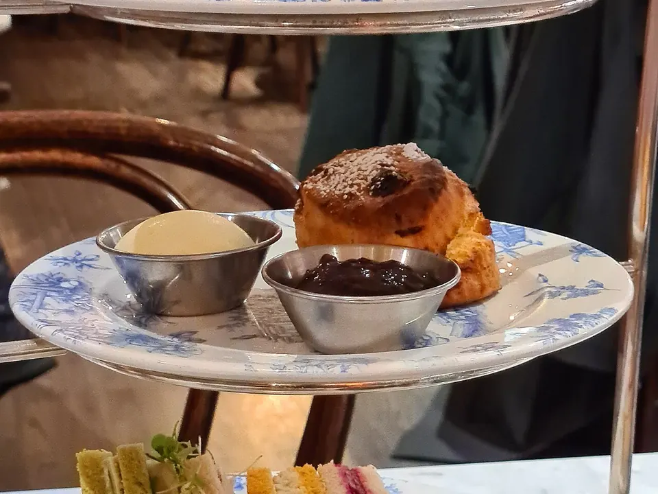 Bandeja de três níveis com sanduíches, scones e doces ao lado de um bule de chá