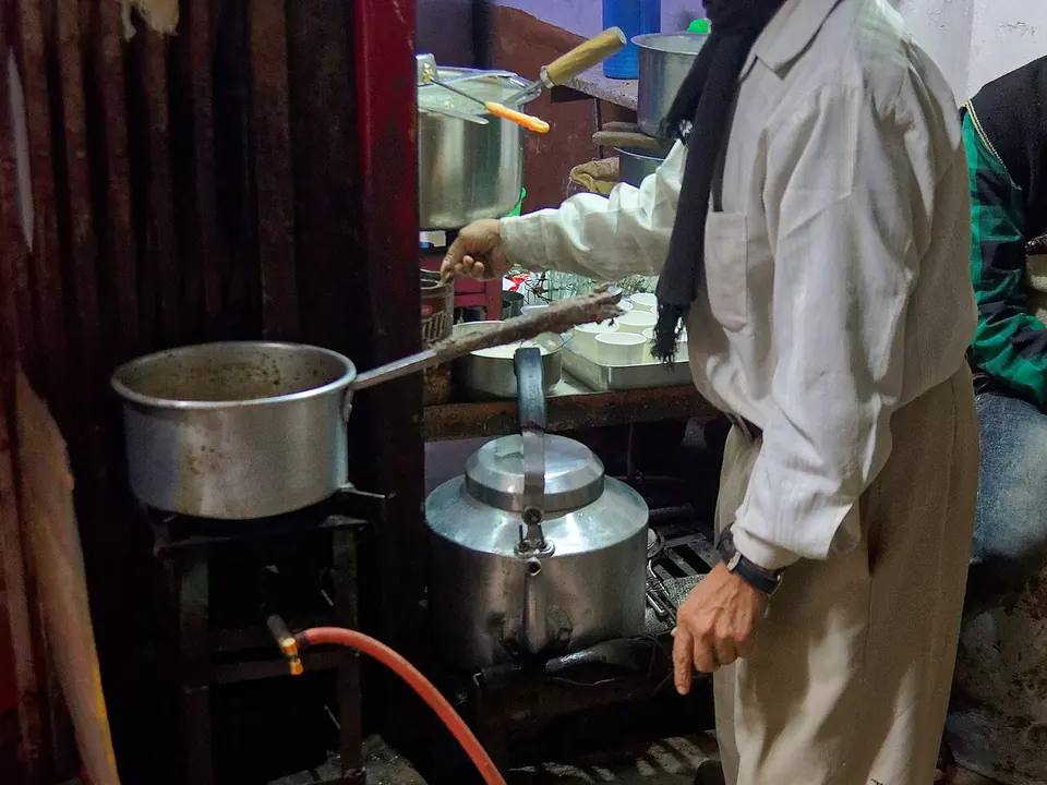 Vendedor de rua despejando masala chai de uma panela em copos de vidro na Índia